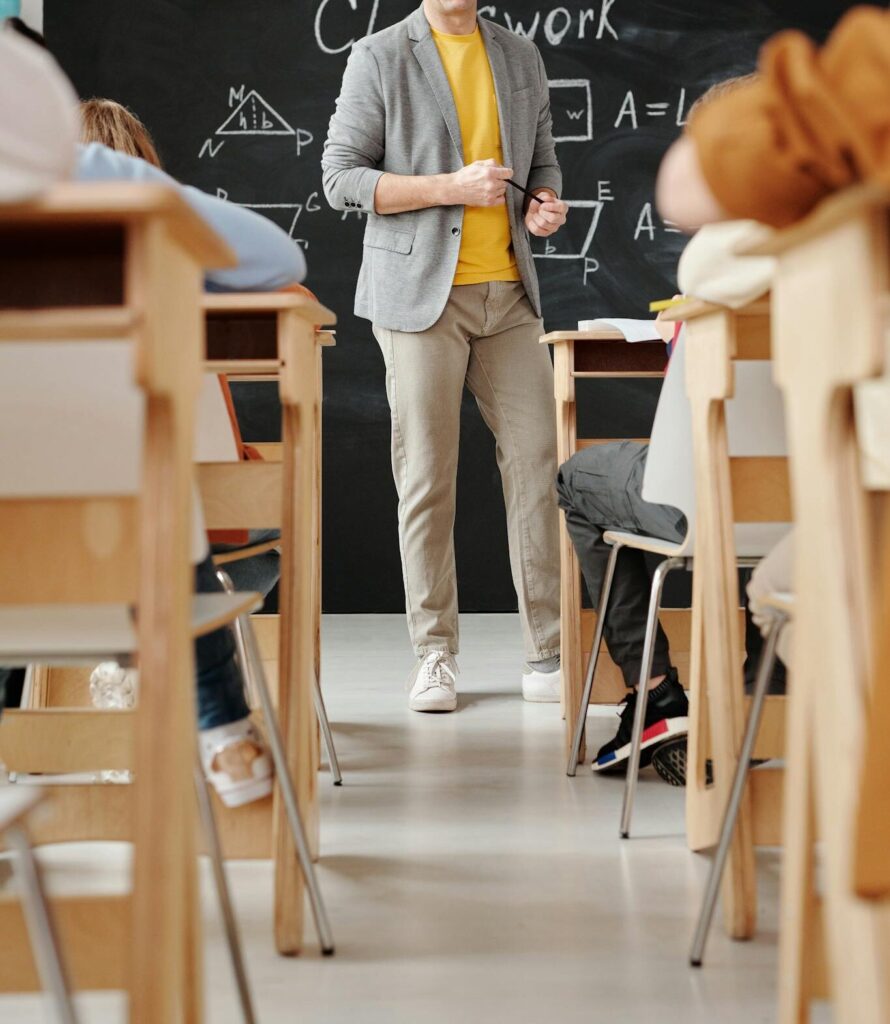 Bald teacher explaining geometry on blackboard to attentive students in classroom.