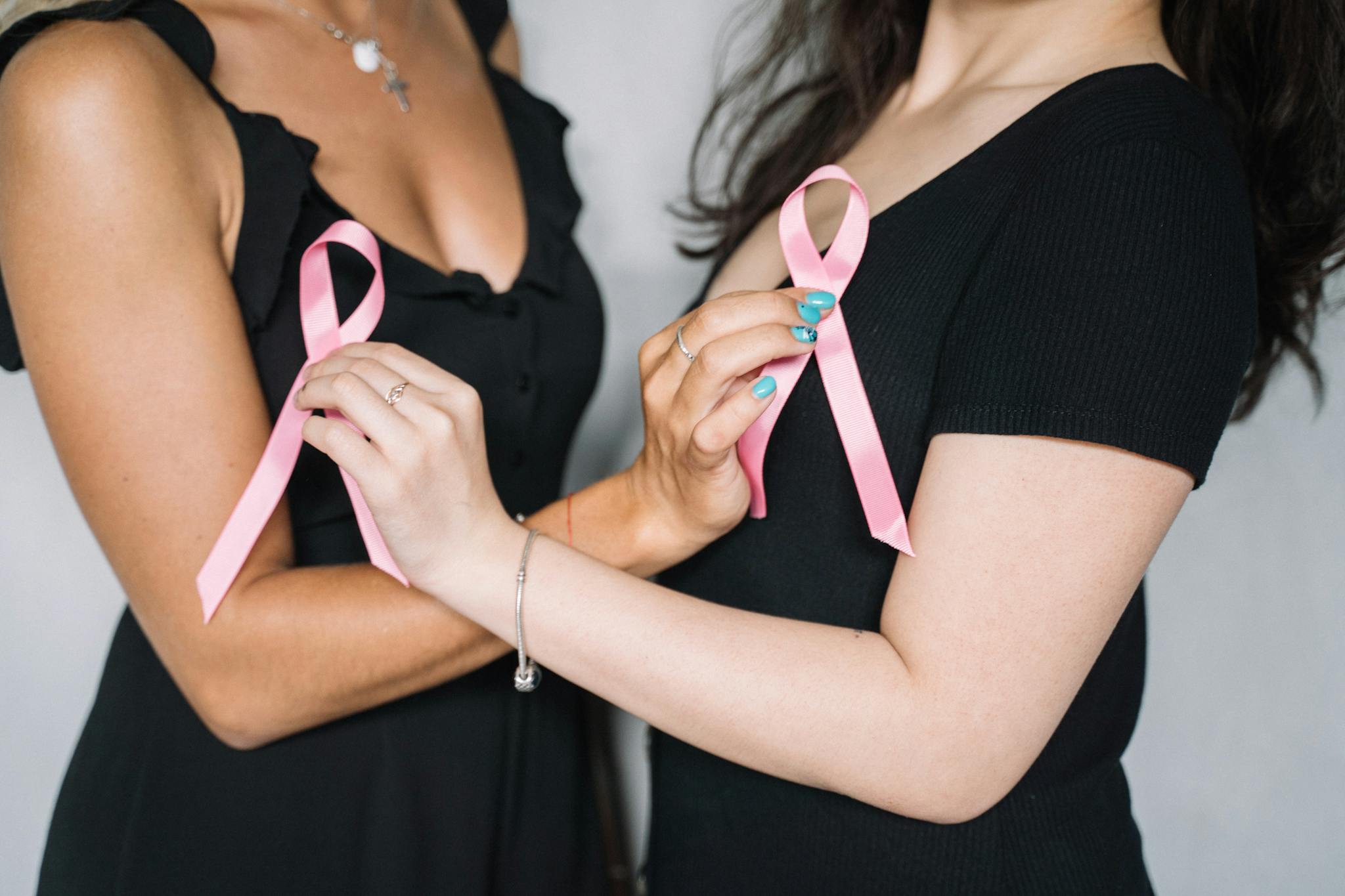 Close-up of two women holding pink ribbons symbolizing breast cancer awareness and support.