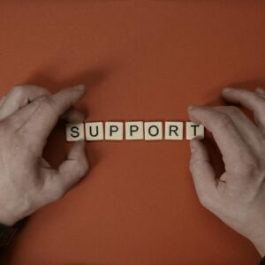 Hands arranging letter tiles to spell the word 'support' on a red background.