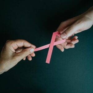 Two hands exchanging a pink ribbon symbolizing breast cancer awareness and support.